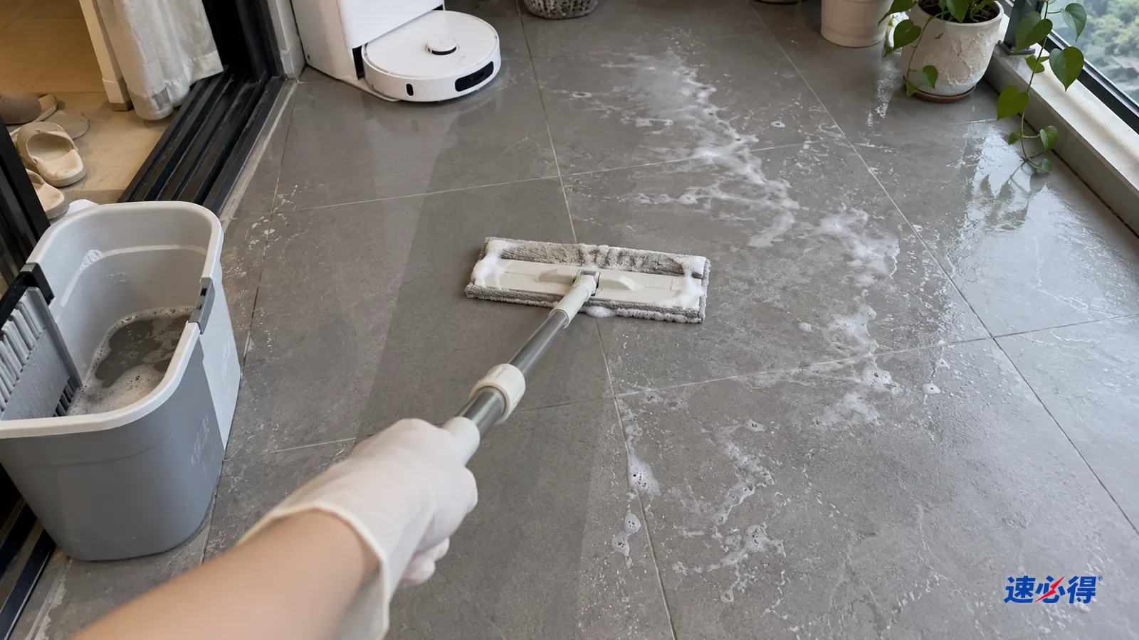 第一人称近拍，戴白色丁腈手套的手握平板拖把，用清水拧干的拖布回拖阳台灰色哑光瓷砖上的发白泡沫痕，拖布边带一点白沫，拖过一条干净，旁边仍有白痕。