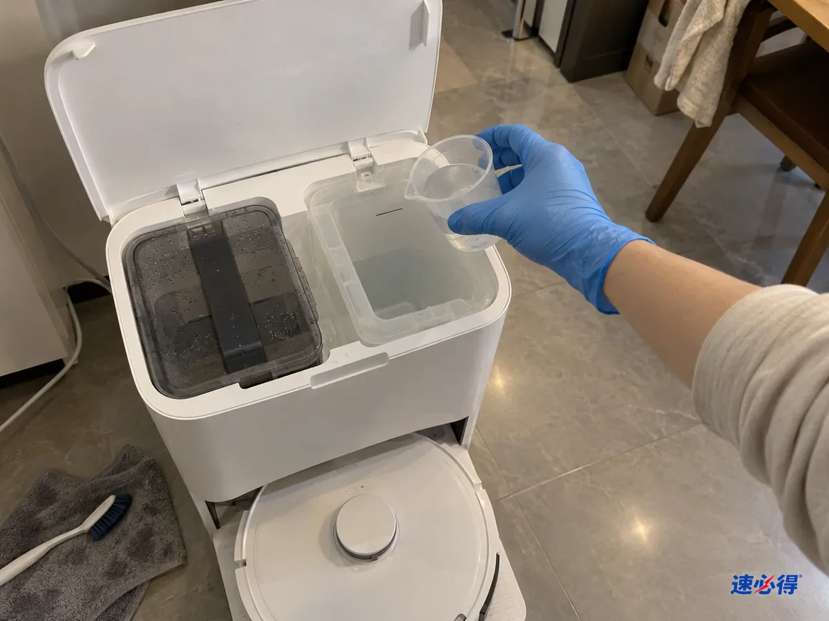 戴蓝色手套的手把小量杯举到掀盖的基站加液仓口上方，对照仓壁上的最高标记