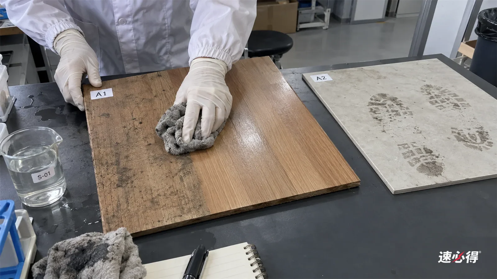 实验台上，戴白色丁腈手套的手用拧干的拖布块擦木地板样板，擦过的一条干净，拖布块上沾着灰色污迹，旁边瓷砖样板还留着灰脚印，量杯放在台边。