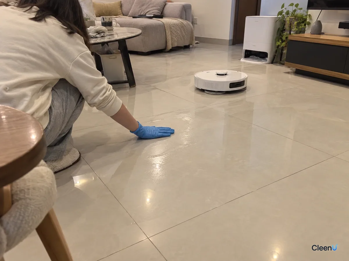 A person kneels and touches a mopped tile floor to check if it is dry while the robot mop works in the living room.