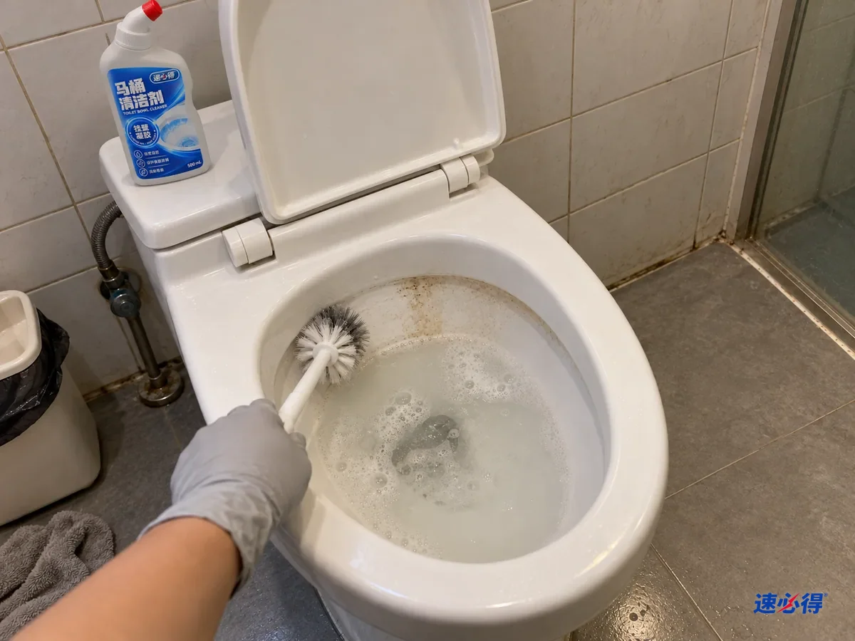 戴浅灰色丁腈手套的手拿马桶刷刷洗马桶内壁的水位线，刷过的一段变白，水面泛灰，一瓶速必得马桶清洁剂盖好立在水箱盖上。