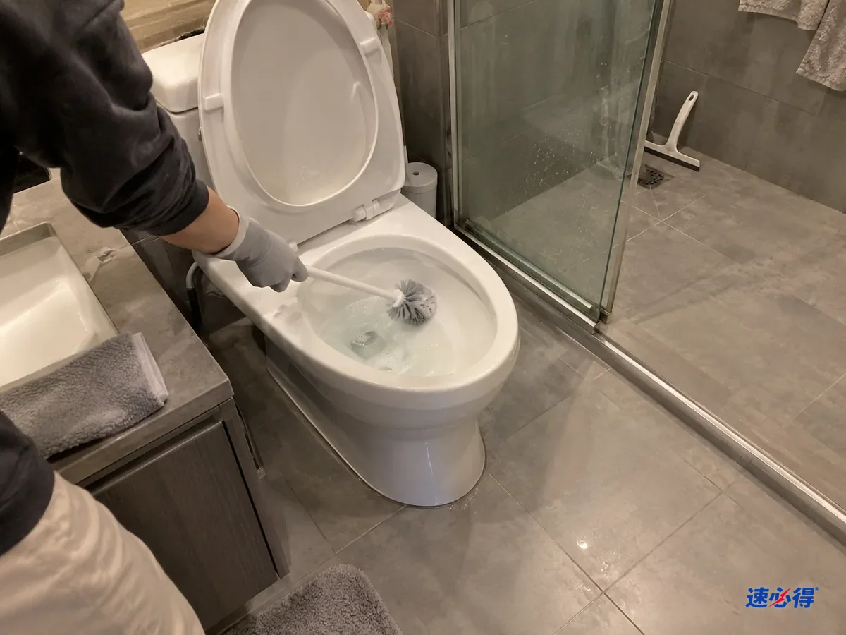 同一个卫生间稍后，戴浅灰色丁腈手套的手用马桶刷刷洗马桶内壁，刷过的一侧白净，洗手台已经擦干。
