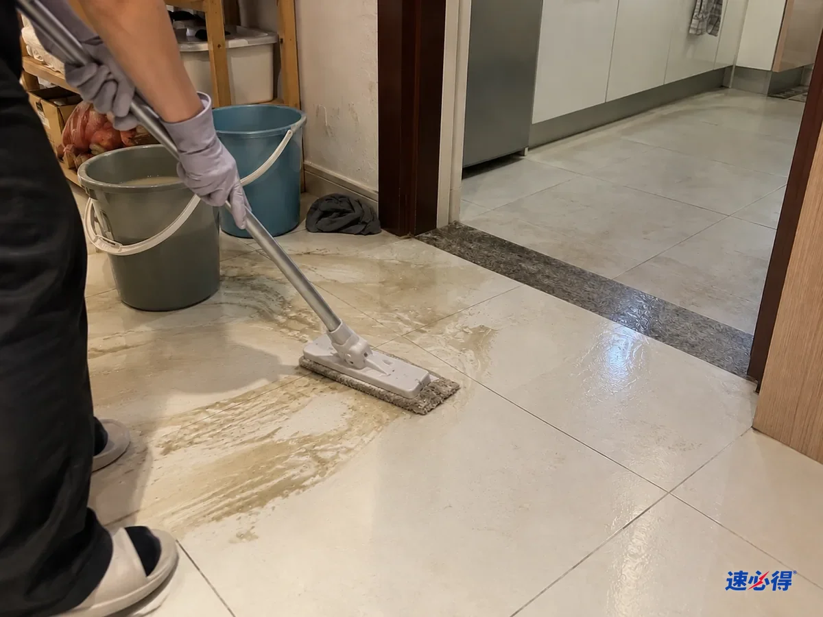 同一处厨房门口，戴浅灰色丁腈手套的手用平板拖把趁湿把刷出的灰黄污水吸走，拖布已经发灰，旁边水桶里是浑水。