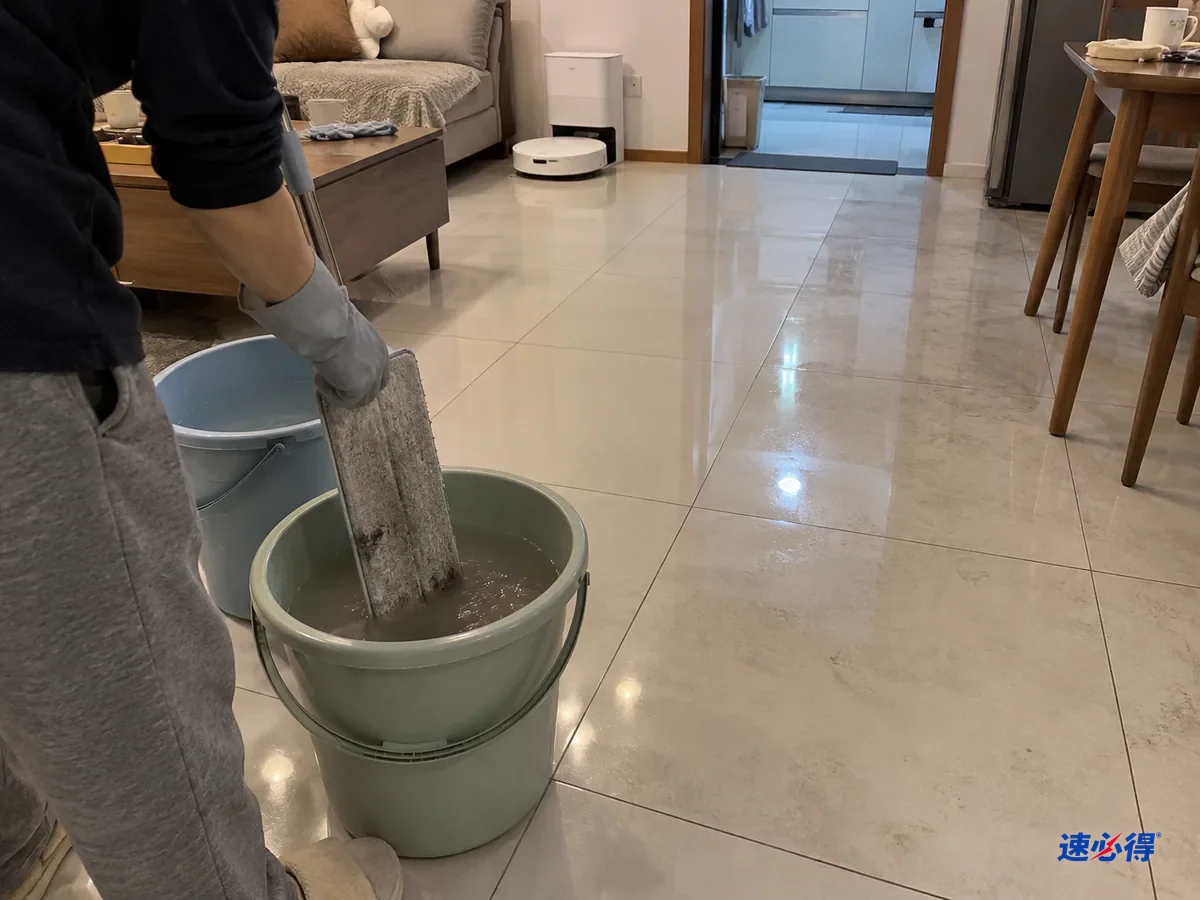一步外看，戴浅灰色丁腈手套的手把发灰的平板拖布在第二只清水桶里涮洗，桶里水变浑，身后客厅瓷砖一半已拖亮，一半仍发灰。