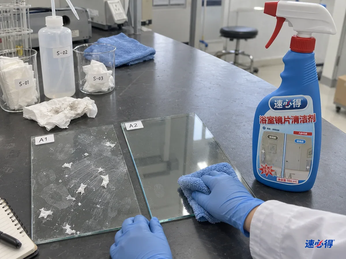 实验台上两块贴着不同测试编号的玻璃样板，都带着油性手印，一块用纸巾擦过后发花、有纸屑，另一块用喷了玻璃清洁剂的超细纤维布擦过后透亮，台面上放着一瓶速必得浴室镜片清洁剂。
