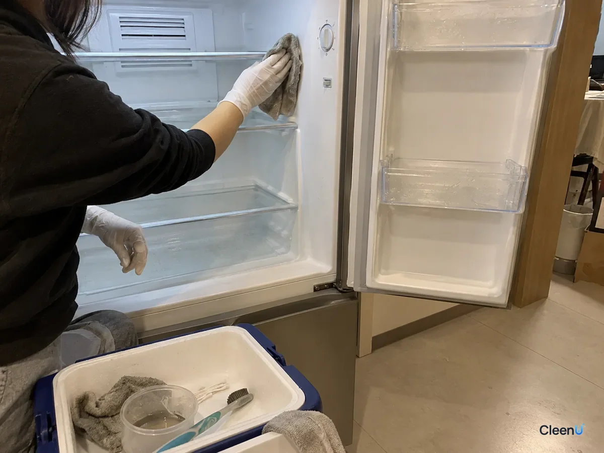 White-gloved hand wiping the fridge side liner with a wrung-out cloth, keeping clear of the nearby temperature control panel and rear air vent