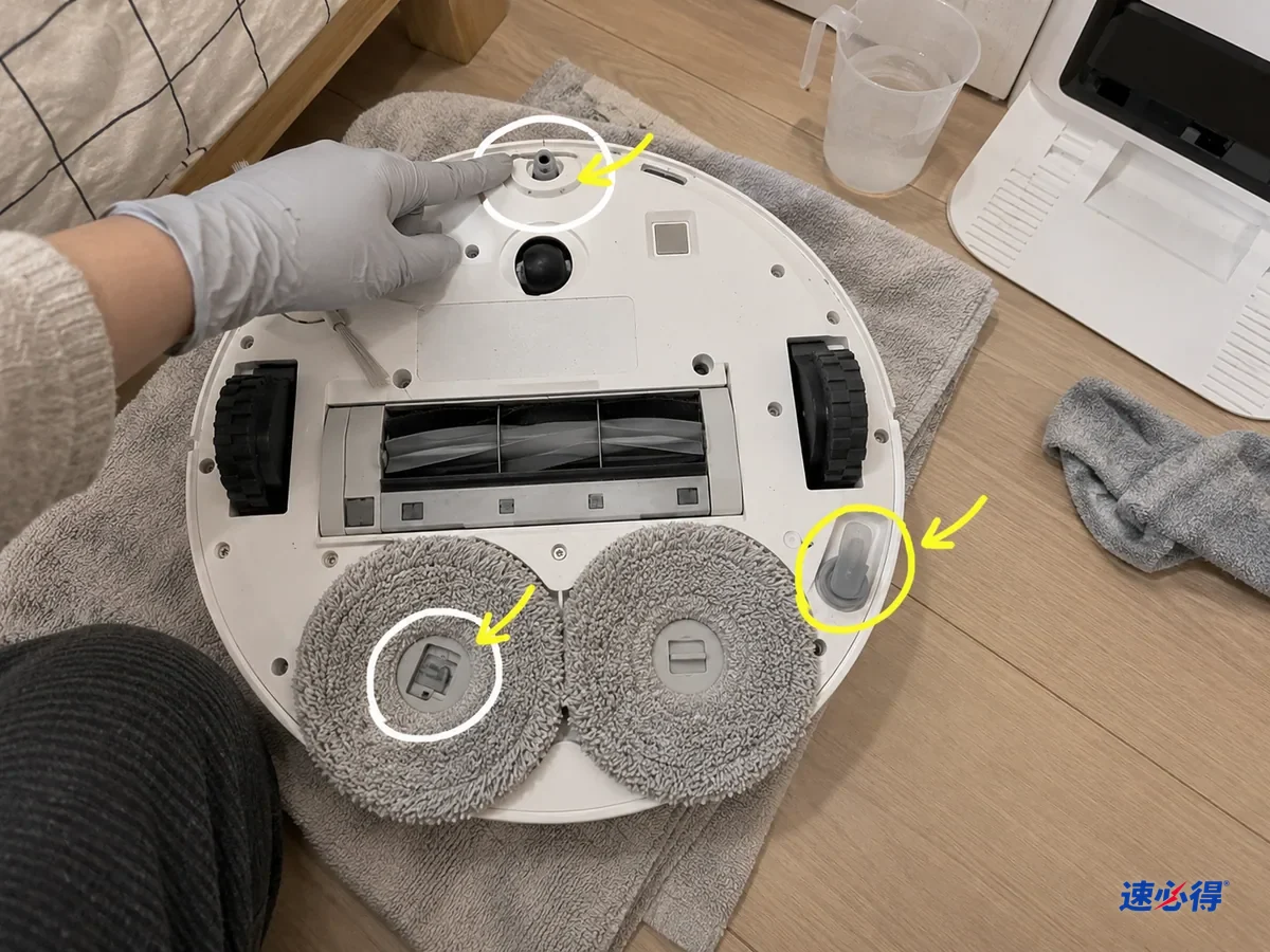 翻过来的扫拖机器人底部，前端喷嘴、拖布垫卡扣和注水口被标出