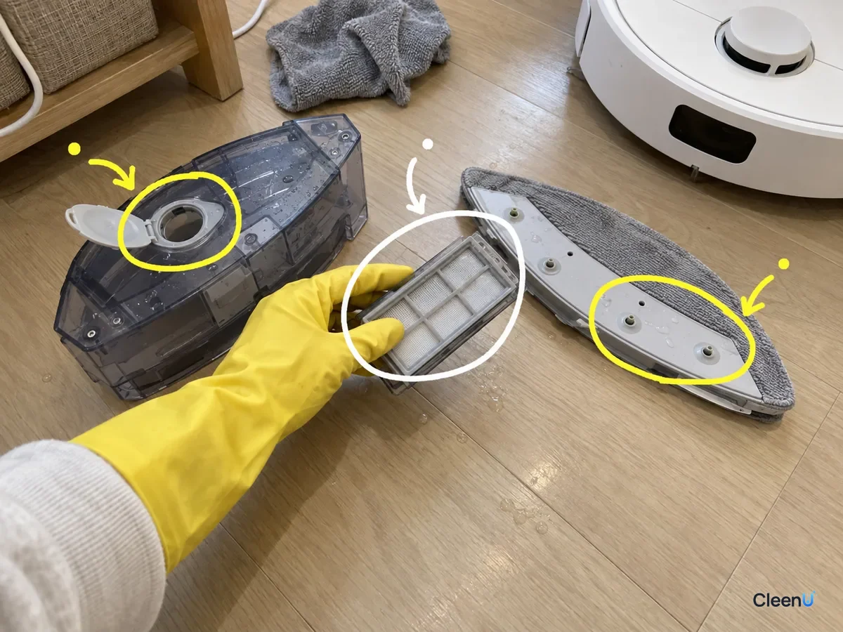 A gloved hand holds a robot mop filter, with the clean tank inlet, filter and mop pad outlet holes marked on the floor.