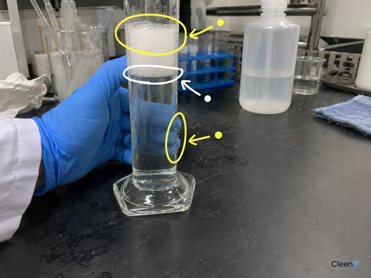 A shaken cylinder with the foam layer, the liquid line under it and bubbles clinging to the glass marked to judge foaming.