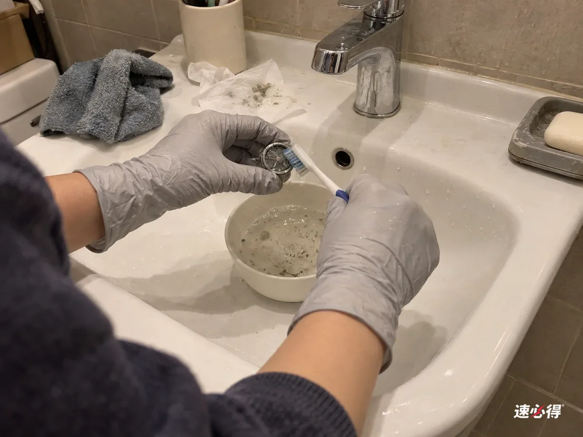 洗手盆边，戴浅灰色丁腈手套的手用旧牙刷刷洗泡过的起泡器网片，网眼里的白色水垢一点点脱落，小碗里的液体有细小残渣。