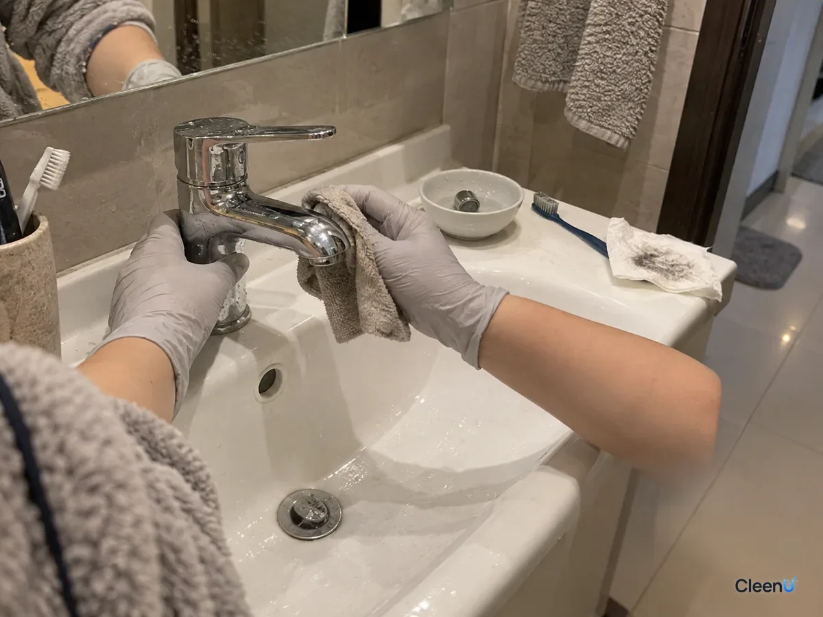 Same basin later: a hand in light grey nitrile gloves dries the rinsed chrome faucet with a soft cloth, the surface bright again, the cleaned aerator waiting beside it to be refitted.