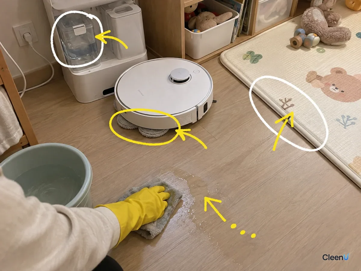 A robot mop near a baby play mat with the dock tank, mop pads and mat edge marked as a hand wipes the floor.