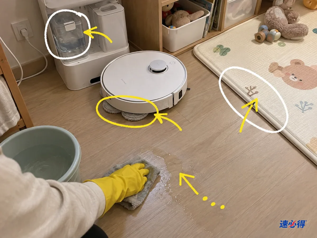 儿童房里基站的清水箱、拖布和爬垫边缘被标出，戴手套的手正擦拭地上的水痕