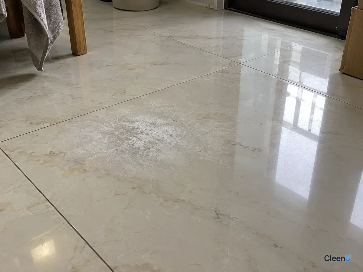 AI illustration: Close-up of a light marble floor with a small patch that has lost its polish and looks dull and white, the surrounding stone still glossy