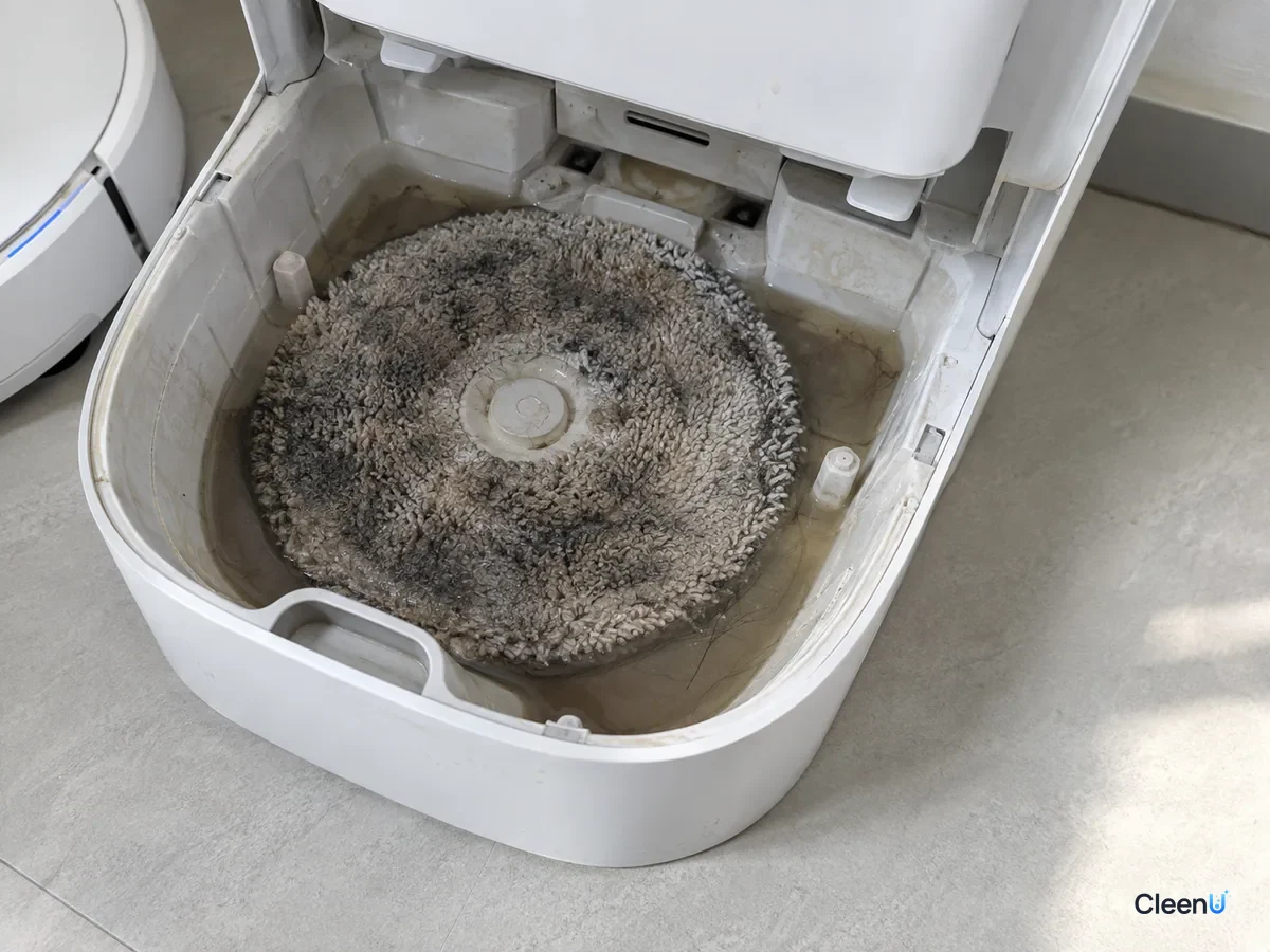 AI illustration: A gray, darkened mop pad sitting in the dock's wash tray, with dirty water and hair collected in the bottom