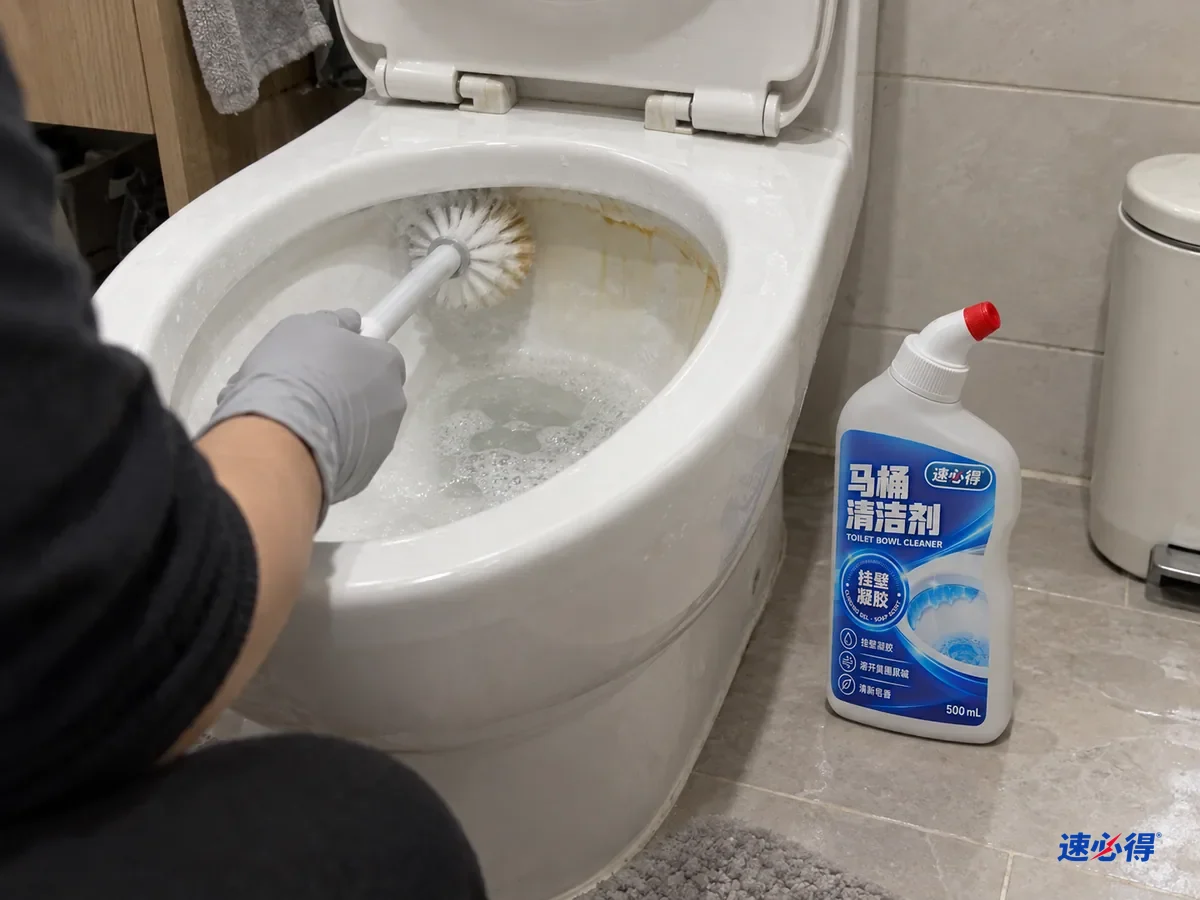 一步外看，戴浅灰色丁腈手套的手拿马桶刷刷洗马桶边缘下方，刷头沾着淡黄色垢屑，一侧已变白，另一侧仍有黄圈，盖好的弯头挤瓶立在马桶边。